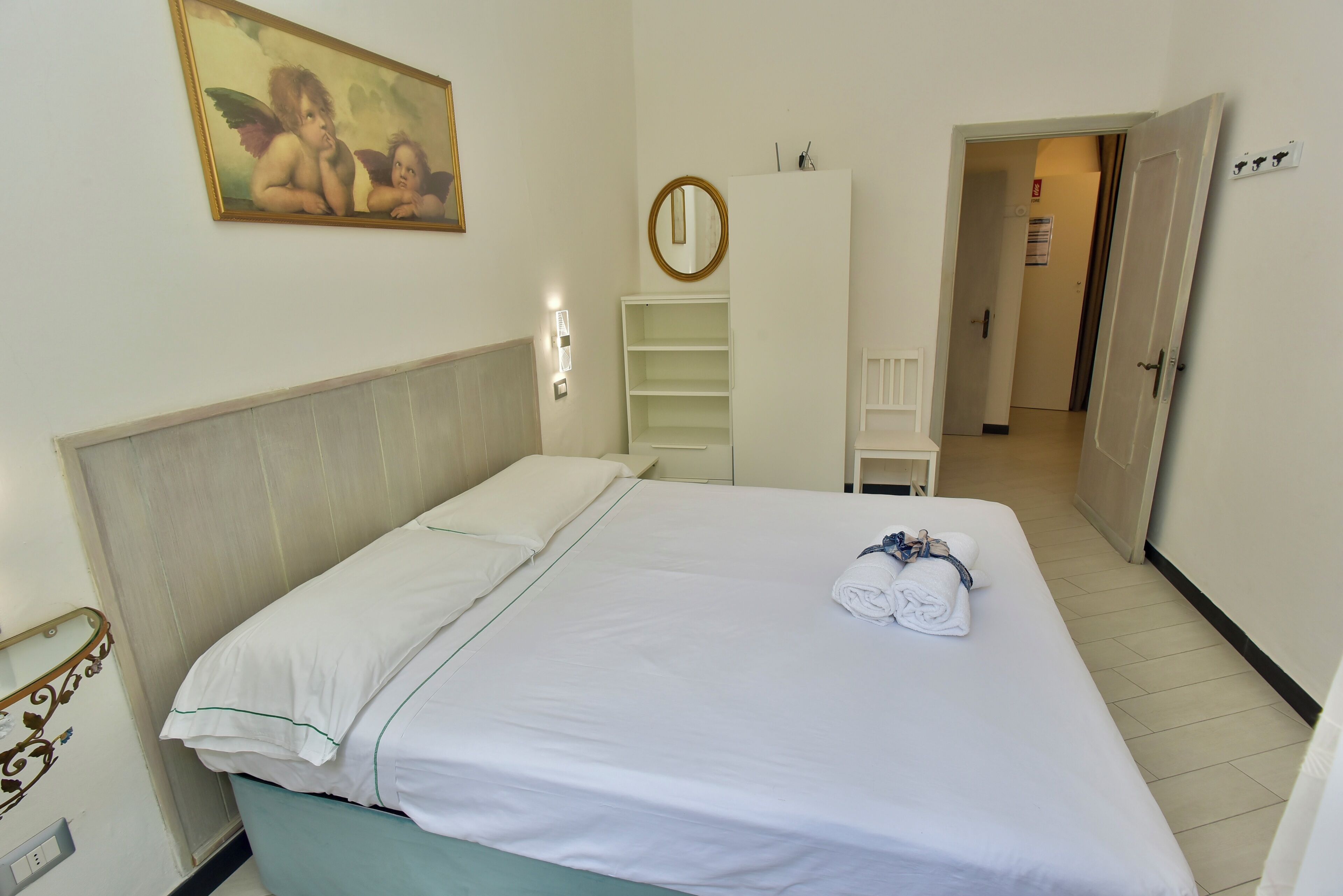 A hotel room with a bed, a painting, a mirror, and a door leading to another room.