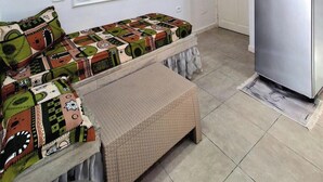 Une cuisine compacte dotée d’un réfrigérateur intégré, d’une étagère où sont exposées des assiettes décoratives et d’un canapé à motifs.