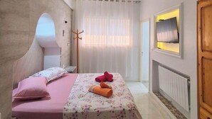 Une chambre avec deux lits, un porte-manteau en bois, une télévision et un radiateur.
