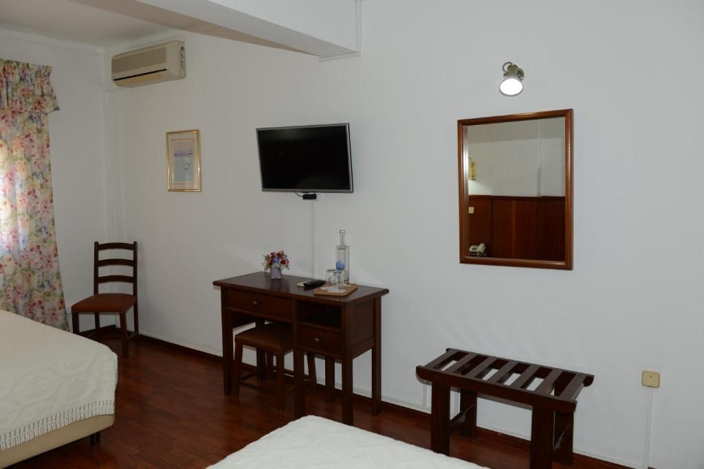 Una habitación con una cama, un escritorio con una silla, un televisor, un espejo y un banco.