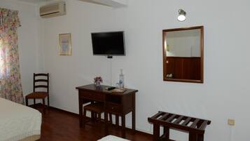 Una habitación con una cama, un escritorio con una silla, un televisor, un espejo y un banco.