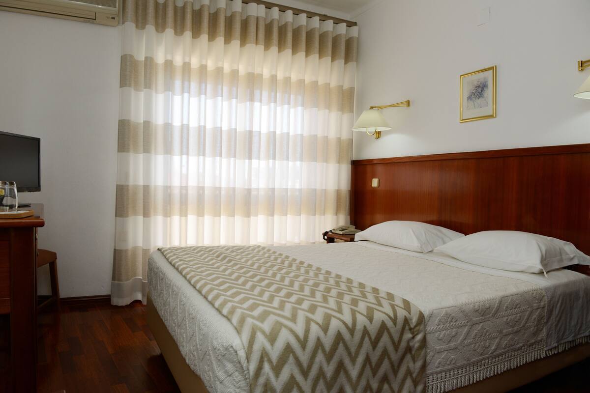 A hotel room with a bed, a desk, a chair, a telephone, and a wall-mounted lamp.
