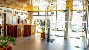 A reception area with a wooden reception desk, a potted plant, and a glass door leading outside. - Estalagem Sequeira (Sao Bras de Alportel)