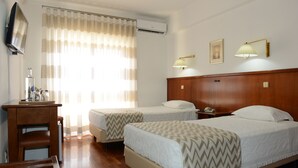 A hotel room with two beds, a desk, a chair, a television, and a window with curtains. - Estalagem Sequeira (Sao Bras de Alportel)
