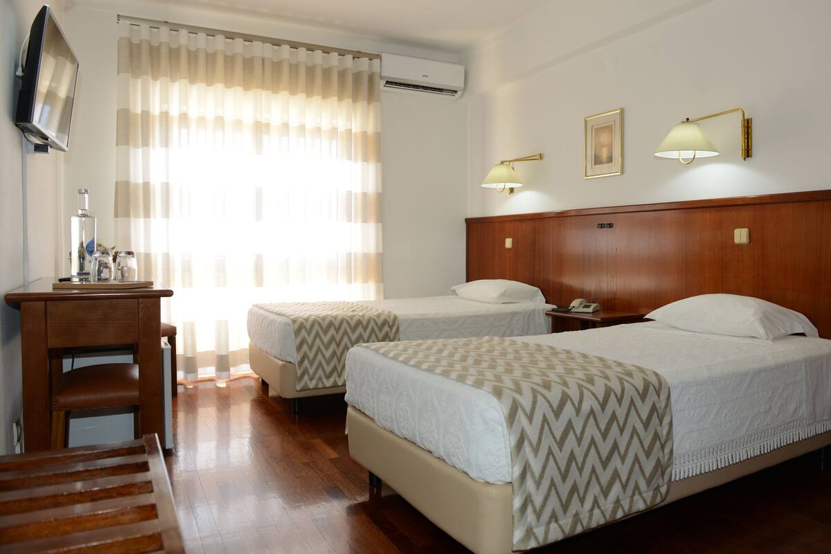 A hotel room with two beds, a desk, a chair, a television, and a window with curtains.