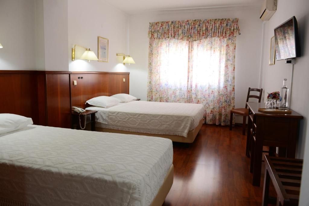A hotel room with two beds, a desk, a chair, and a television.