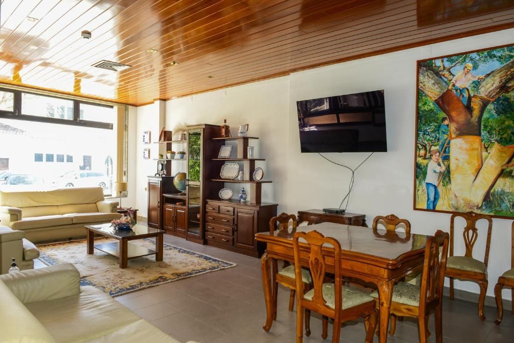 A living room with a sofa, coffee table, wooden dining table, chairs, a TV mounted on the wall, and a bookshelf.