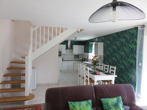 A modern kitchen with white cabinets, a dining area with a white table and chairs, and a staircase with wooden steps.
