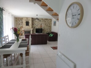 A living room with a stone wall, a fireplace, a television, and a large wall clock.