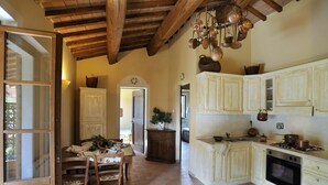 Une cuisine avec des meubles de rangement en bois, une table à manger avec des chaises et un porte-casseroles suspendu.