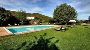 Une piscine dotée de chaises longues et d’un kiosque, le tout entouré d’une pelouse bien entretenue et d’arbres.