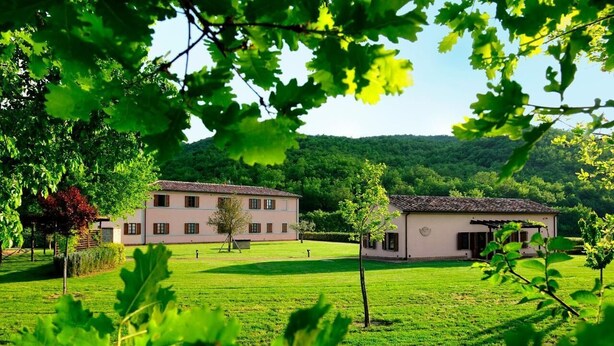 Un grand bâtiment avec un jardin à l’avant, entouré d’arbres et de collines.