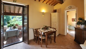 Un coin repas avec une table dressée pour deux personnes, un buffet en bois et une vue sur le jardin par une porte ouverte.