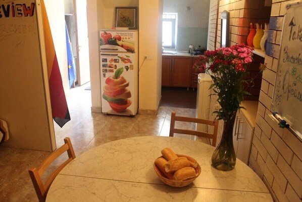 A kitchen with a marble countertop, a dining table with chairs, a refrigerator with magnets, and a vase with flowers.