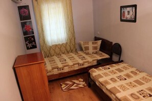 A small bedroom with two single beds, a wooden nightstand, a patterned rug, and a wall-mounted air conditioning unit.