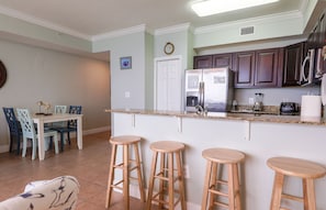 A modern kitchen with a central island, bar stools, and a dining area with chairs.