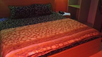 A bed with patterned bedding, a nightstand with a phone, and a wall-mounted light fixture.