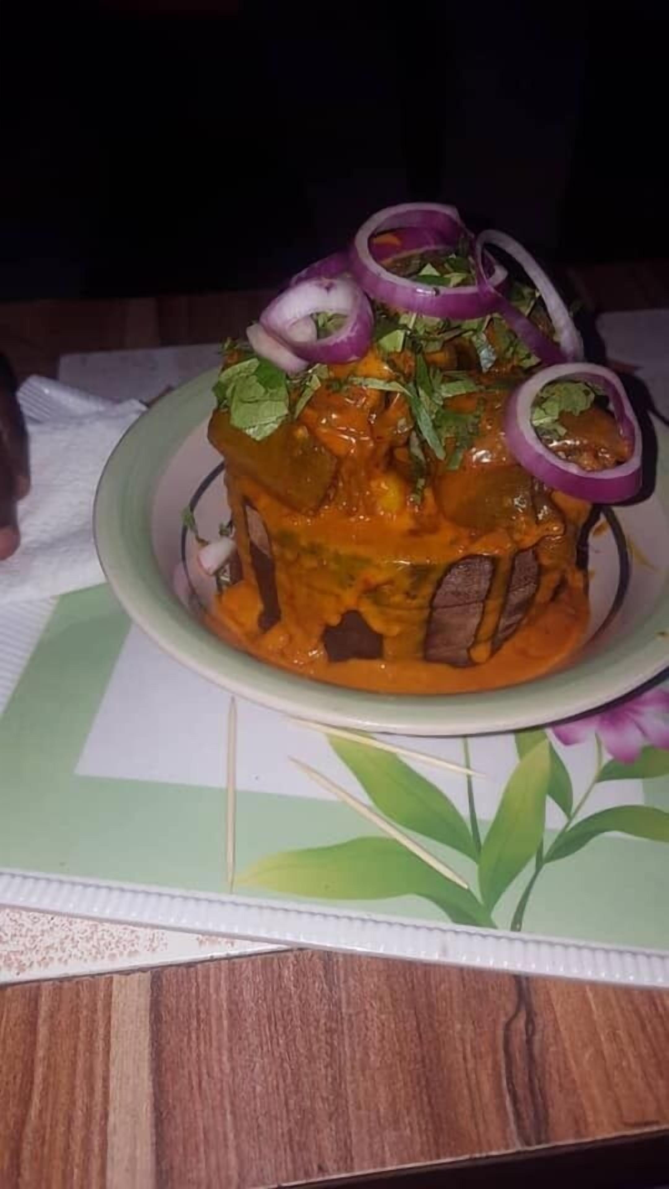 A dish with a rich orange sauce, garnished with slices of red onion and green herbs, served on a plate with a floral design.