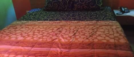 A bed with patterned bedding, two wall-mounted lights, and a small bedside table with a phone.