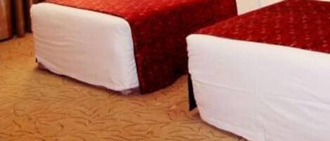 Habitación de hotel con dos camas, cada una con cubrecama rojo y almohadas blancas.