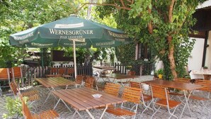 Et udendørs siddeområde med træborde og bænke, overdækket af en stor, grøn parasol med 'Wernesgruen' branding.