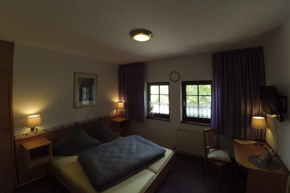 Una habitación de hotel con cama, lámparas de noche, escritorio y ventana con cortinas.