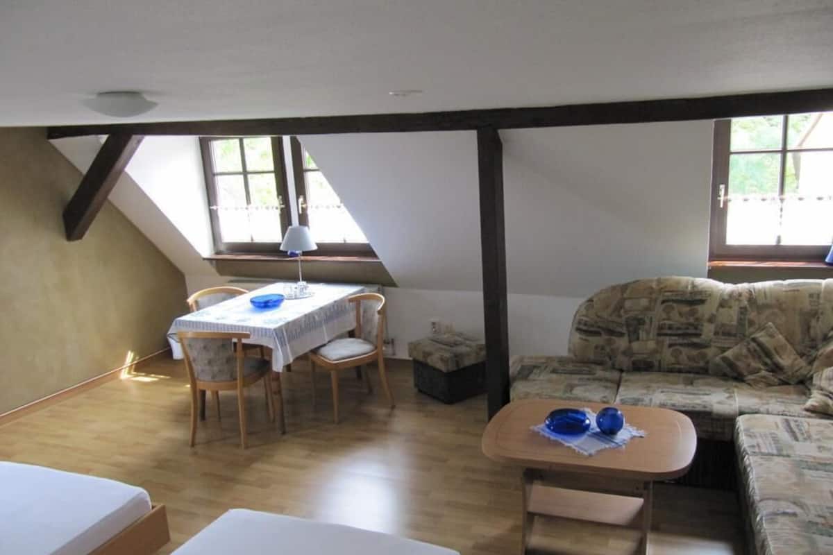Una habitación con techo inclinado, una mesa de comedor con sillas, un sofá y una mesita con una lámpara.