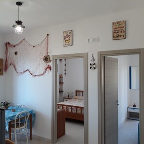 A room with a bed, a desk, and a chair. There are two doors, one leading to another room and another to the outside. - Central apartment with sea view 150 meters from the Bellavista Residence beach (Marina di Camerota)