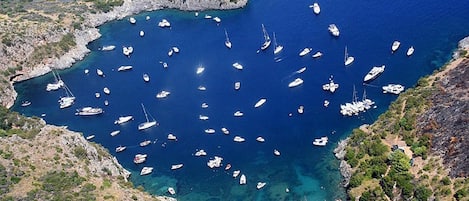 A coastal area with numerous boats anchored in a bay surrounded by rocky terrain and sparse vegetation.