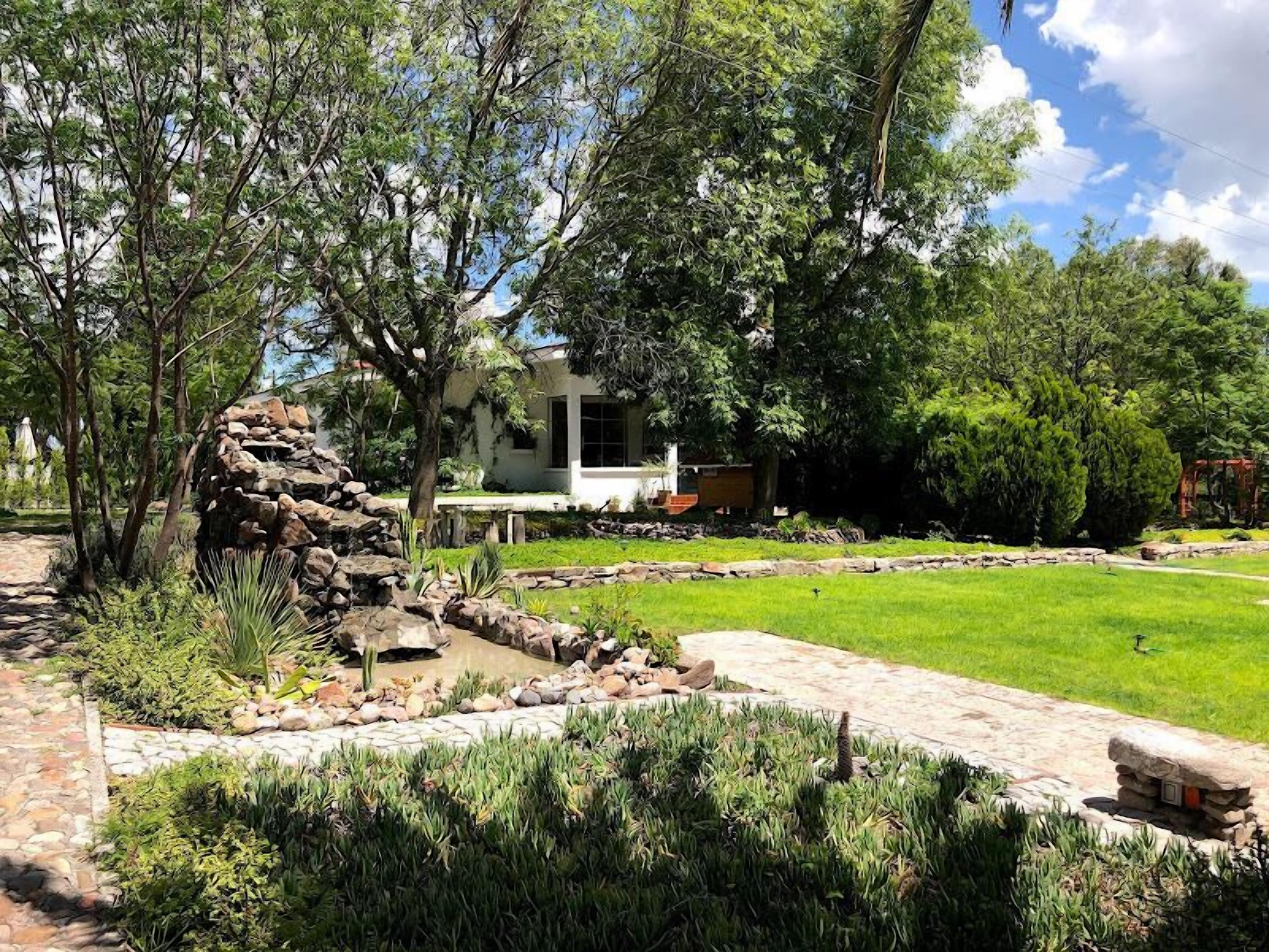 A landscaped garden with a stone wall, a grassy lawn, and a white building with a window.