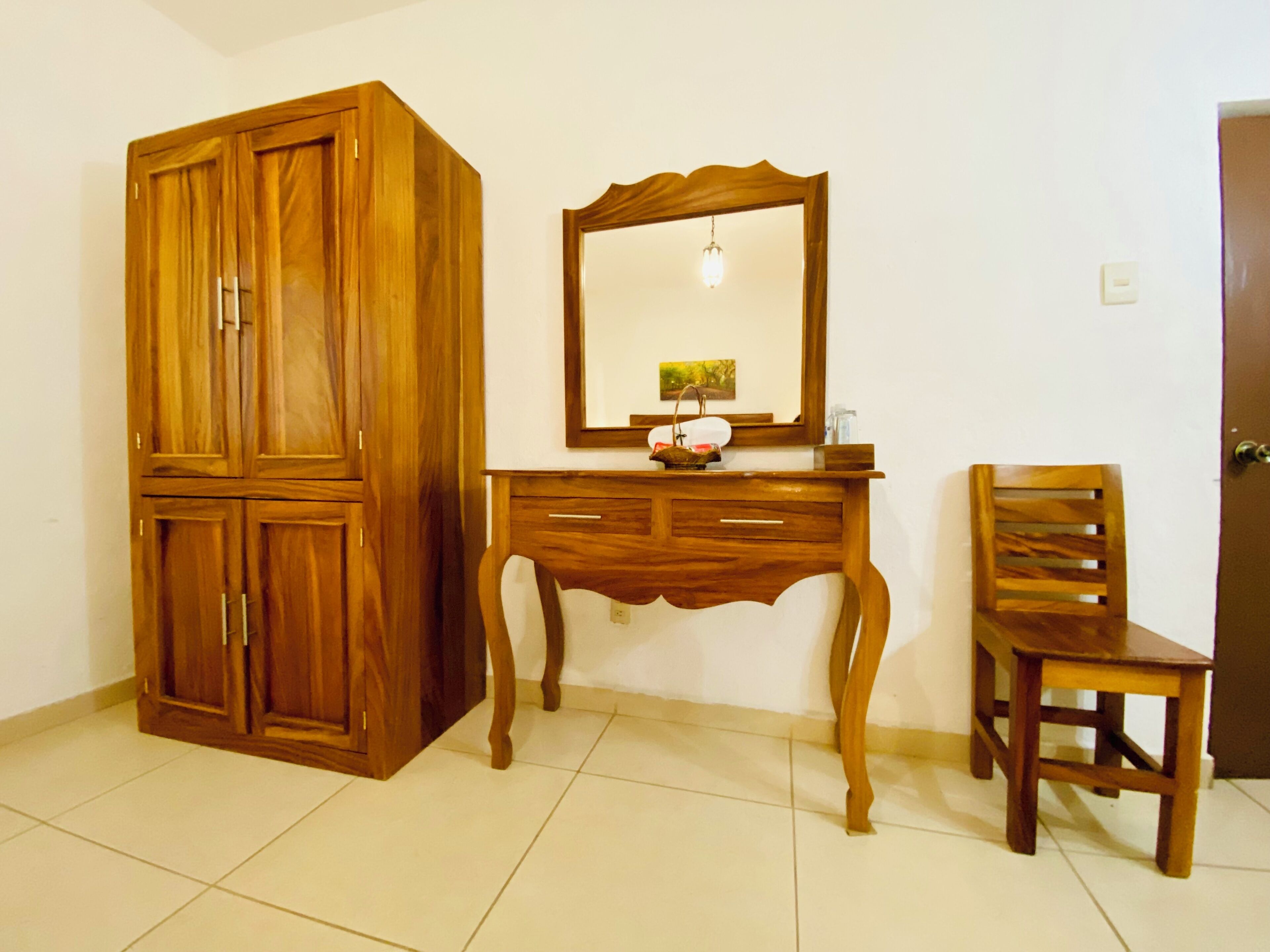 A room with a wooden wardrobe, a wooden desk with a mirror, and a wooden chair.
