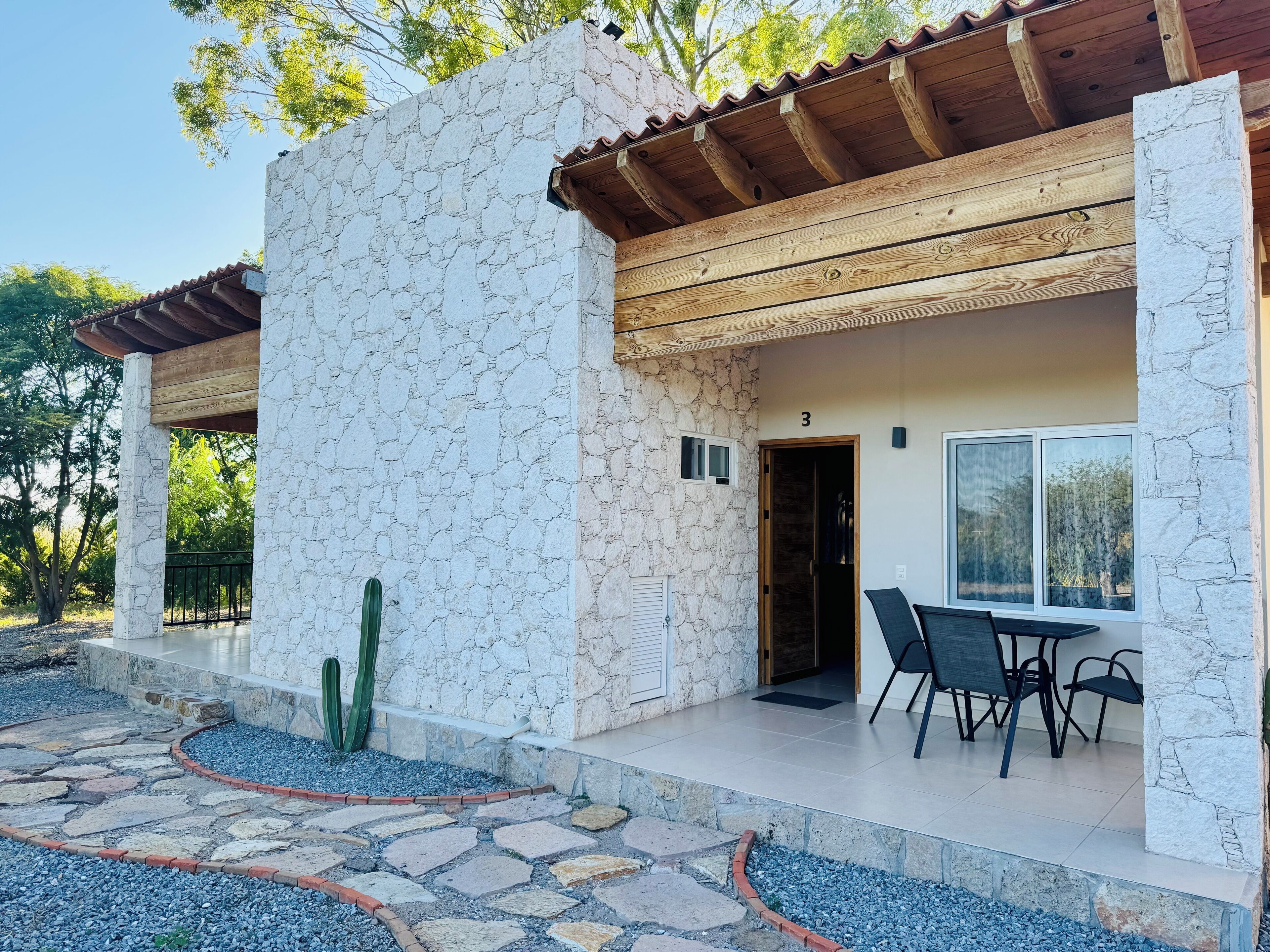 Un edificio de piedra con techo de madera, una puerta numerada con el número 3, y un patio con mesa y sillas.