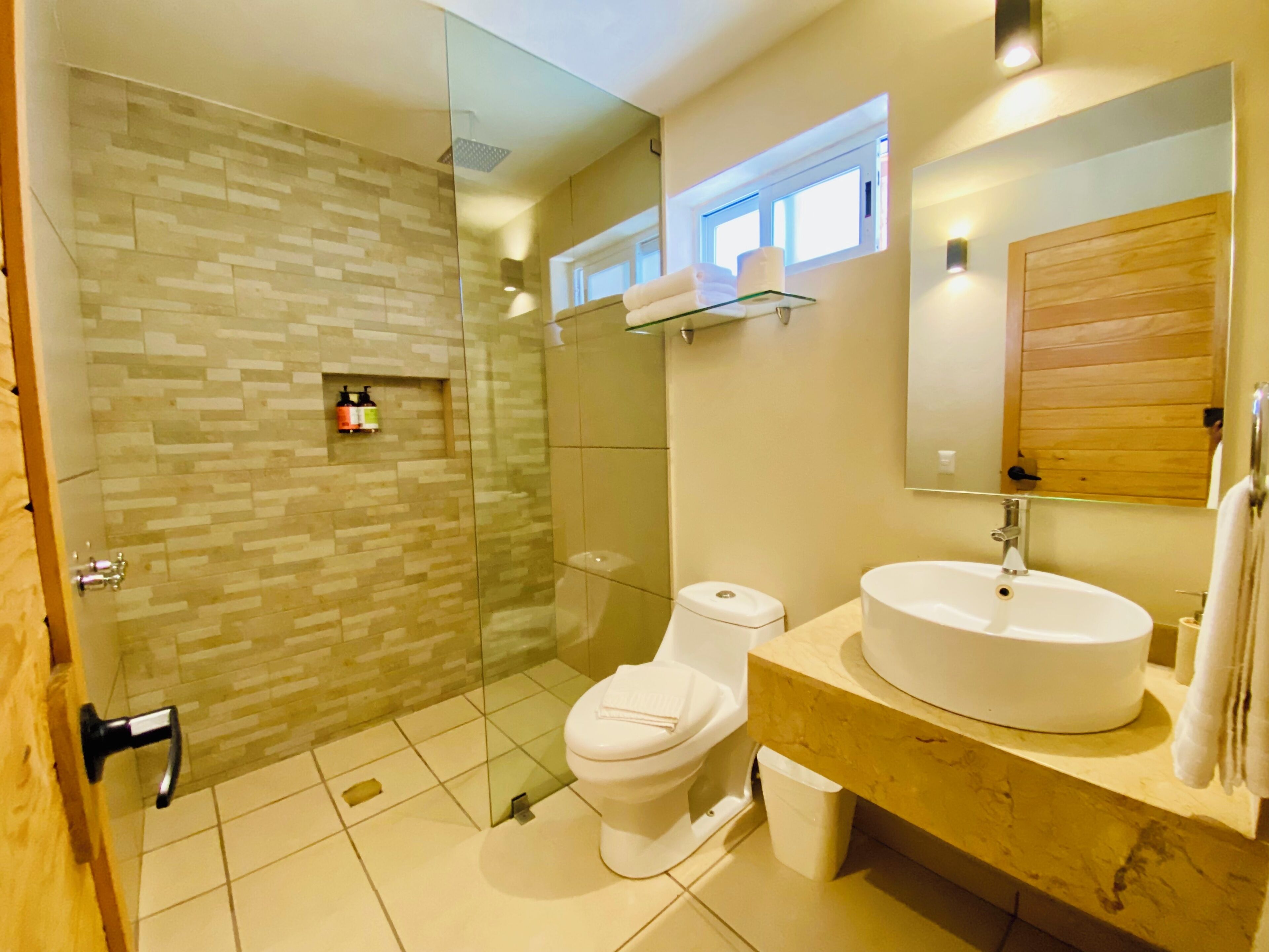 Un baño moderno con ducha de vidrio, inodoro, lavamanos y espejo.