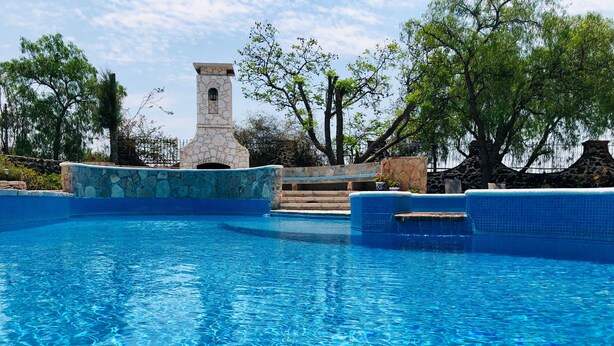 A clear blue swimming pool with stone steps leading up to a stone tower. - Club Vergel Resort (Ezequiel Montes)