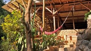 A wooden structure with a thatched roof, stone steps, and a hammock. - Hostel Cascada Verde (Bahía Ballena)