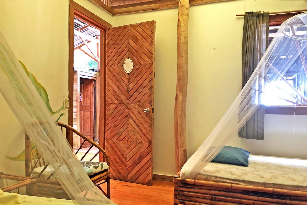 A room with a bed, a chair, a wooden door, and a window with a curtain.