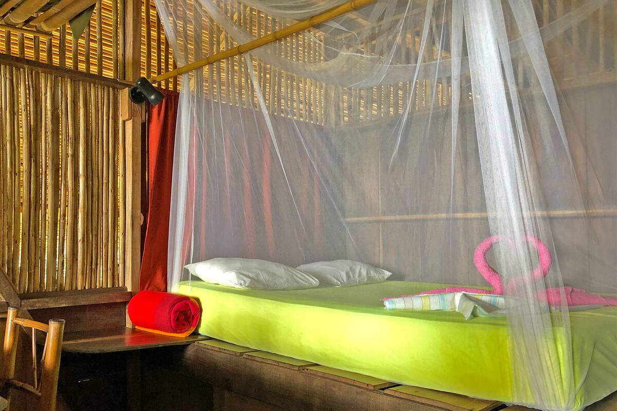 A room with a bed covered by a mosquito net, a wooden headboard, and a red rolled-up item on the nightstand.