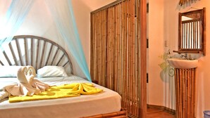 A bed with a canopy, a bedside table, and a wall-mounted sink with bamboo decor. - Hostel Cascada Verde (Bahía Ballena)