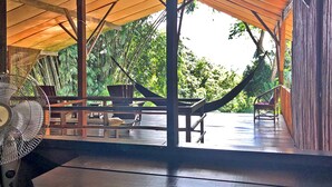 A covered outdoor area with a hammock, tables, and chairs, surrounded by lush greenery. - Hostel Cascada Verde (Bahía Ballena)
