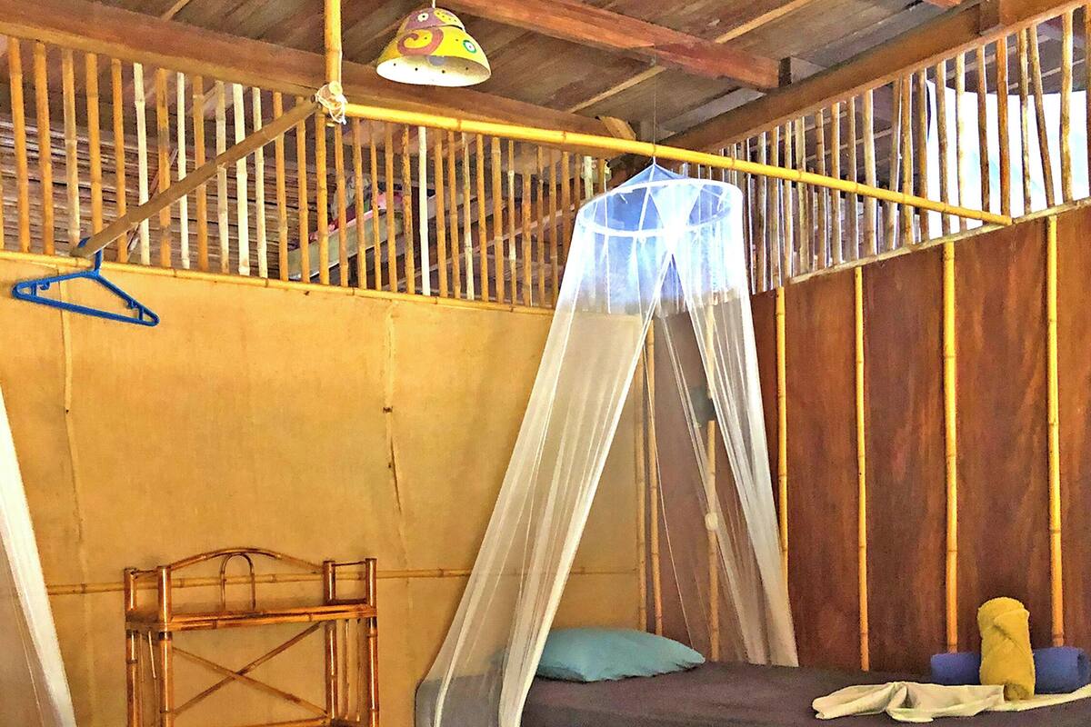 A room with two wooden beds, a hanging chair, and a mosquito net.