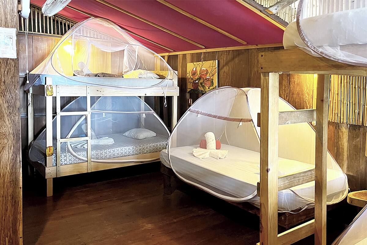 A room with bunk beds, each with a mosquito net, wooden flooring, and a red ceiling.