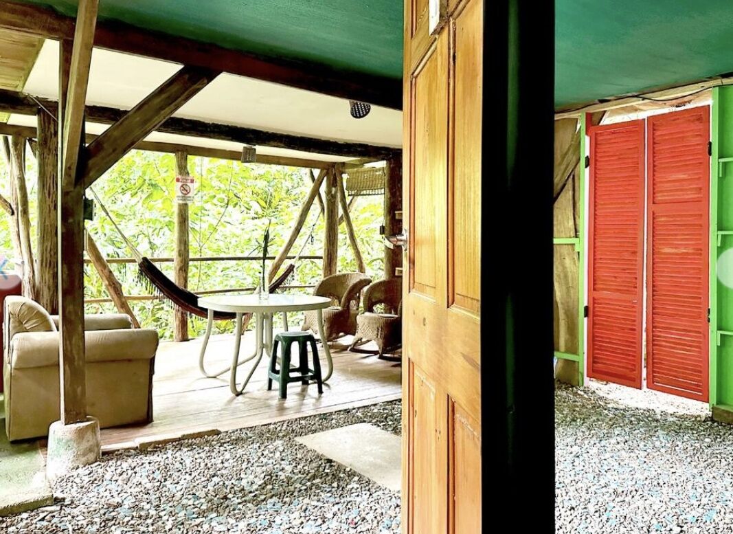 A wooden structure with a covered patio area, a round table, and chairs.