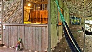 A room with a wooden floor, a bed with a canopy, a hammock, and a wall with a mural. - Hostel Cascada Verde (Bahía Ballena)