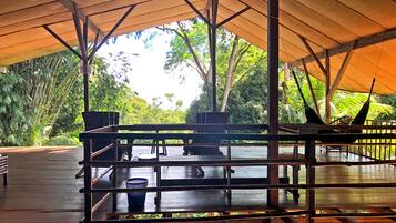 Um deck de madeira ao ar livre com toldo, cercado por vegetação exuberante e árvores.