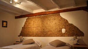Una habitación con dos camas, una pared de ladrillo, vigas de madera y una pequeña mesa con lámpara.