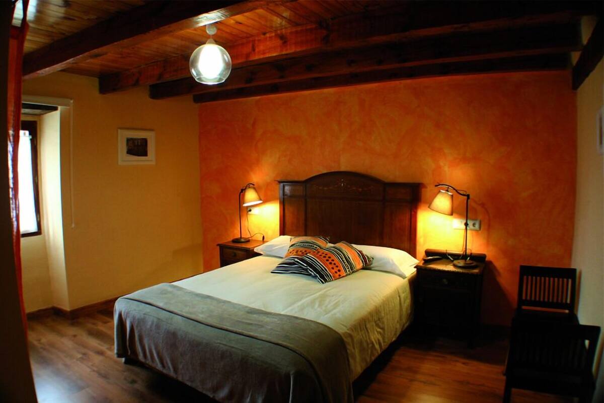 A bedroom with a wooden headboard, two bedside lamps, a bed with a striped pillow, and a chair.