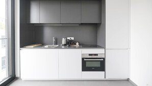 Una cocina moderna con armarios blancos, un lavamanos de acero inoxidable, horno empotrado y una ventana que deja entrar luz natural.