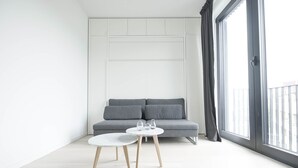 Una sala de estar moderna con un sofá gris, una mesita blanca pequeña y un ventanal con cortinas.