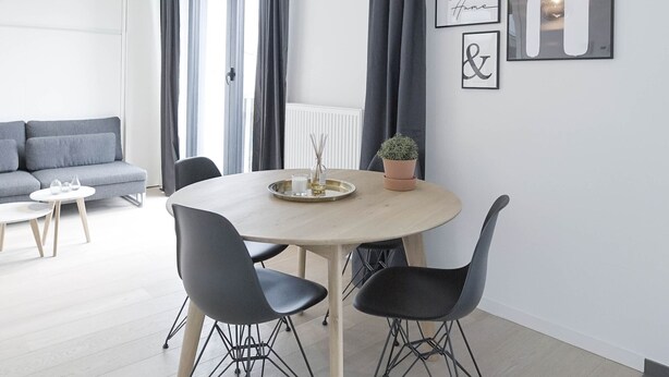 Un comedor moderno con una mesa redonda, dos sillas negras y una lámpara colgante.