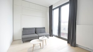 Una sala de estar moderna con un sofá gris, una mesita blanca y un amplio ventanal con cortinas.
